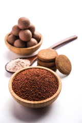 Nachni / Ragi laddu and biscuits or cookies made using  finger millet, sugar and ghee. It's a healthy food from India. Served in a bowl or plate with raw whole and powder. Selective focus