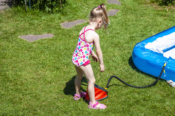 Little girl blowing up inflatable swimming pool