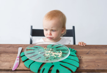 The little girl looks with grief at empty and dirty dessert dish on wooden table