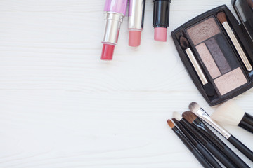 Makeup brush and decorative cosmetics on a pastel pink background with empty space.