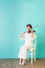 teenager in white outfit playing violin and sitting on chair, on blue © LIGHTFIELD STUDIOS