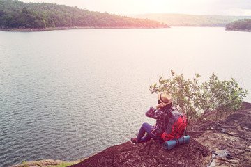 Young hipster woman with backpacker sitting on stone enjoying lake and mountain beautiful landscape view.