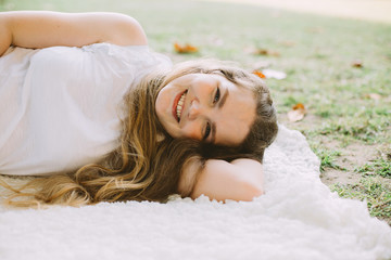 Beautiful young woman smiling lying on white plaid at summer picnic