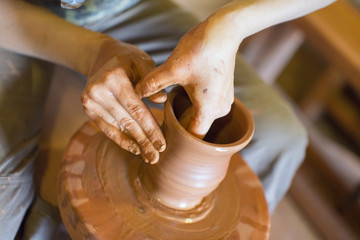 Rotating potter's wheel and clay ware on it taken from above. Hands in clay. Pottery male ceramist creates a hand made clay product. Process of rotation of potter's wheel, hands of ceramist
