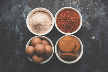 Nachni / Ragi laddu and biscuits or cookies made using  finger millet, sugar and ghee. It's a healthy food from India. Served in a bowl or plate with raw whole and powder. Selective focus
