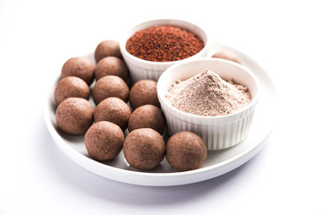 Nachni laddu or Ragi laddoo or balls made using  finger millet, sugar and ghee. It's a healthy food from India. Served in a bowl or plate with raw whole and powder. Selective focus