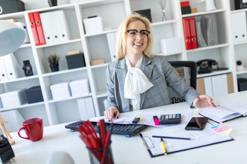 Young girl with glasses works in the office with documents, calculator and computer.