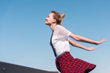 side view of happy young woman with wide arms standing against blue sky