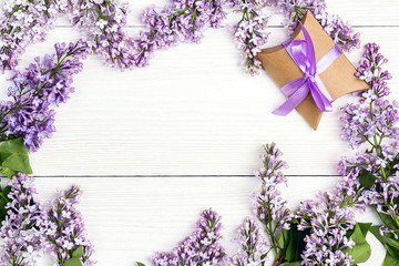 Frame of  lilac flowers with gift box on white wooden background. Copy space.