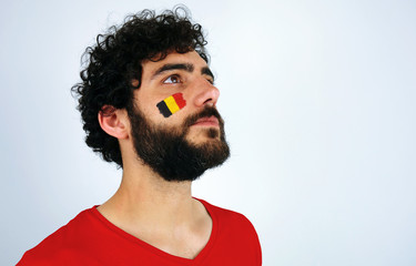 Sport fan head high and feeling proud when listening to the anthem of his country. Man with the flag of Belgium makeup on his face and red t-shirt.   - Powered by Adobe