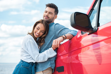 cheerful young couple hugging near red car
