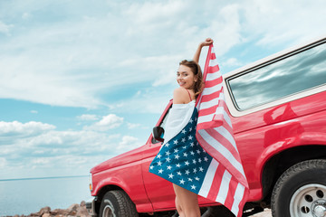 happy beautiful girl with american flag standing near red car