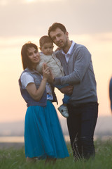 Portrait of a young couple with a child having fun in nature, sunset