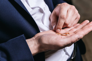 groom holds the wedding rings on the palm