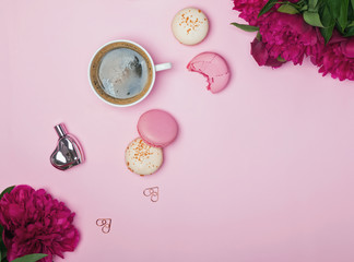 Pink peonies, coffee and french macarons on pastel pink background