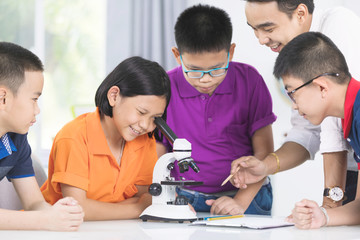 Asian teacher expanding to student in biology class with microscope .