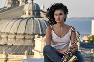 Young woman with saxophone on the roof of a high building