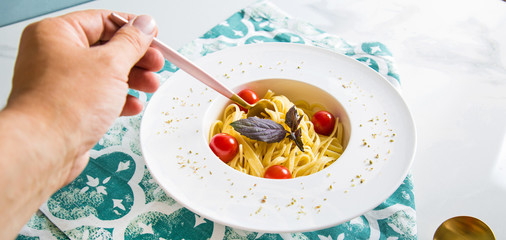 Traditional italian pasta with tomatoes and basil in plate with fork and hand