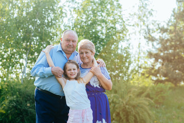 Naklejka na ściany i meble family, love, generation and people concept - happy smiling grandmother, grandfather and little granddaughter hugging together at summer yard or park