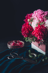 bouquet of pink peonies with scissors, ribbon and vintage bowl with petals on dark