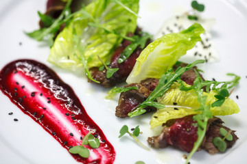 marinated slices of beef with cranberry sauce on white plate for restaurant menu