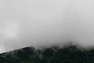 Fog moving over the top of dark green mountain