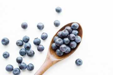 Fresh blueberries in a wooden spoon on a light surface of a table. Closeup, top view.