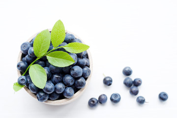 Fresh blueberries in a wooden cup on a light surface. Closeup, top view.