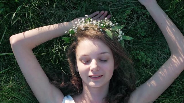 SLOW MOTION: Top view shot of a Caucasian girl in a white floral dress lying in grass