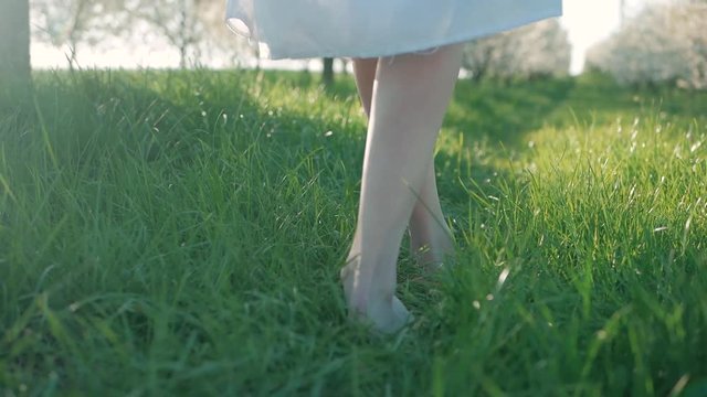 Slow motion shot of bare feet of young girl walking and running on green grass