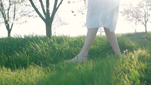 Slow motion shot of bare feet of young girl walking and running on green grass