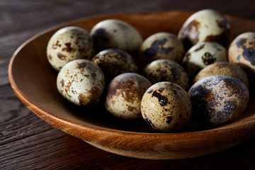 Fresh quail eggs in a wooden bowl on a dark wooden background, top view, close-up