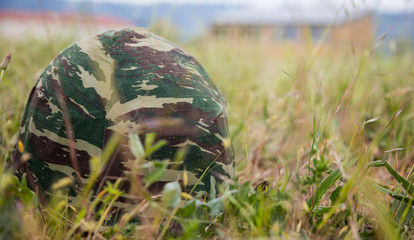 Army camouflage helmet putted down on the ground. Close up front view, blurred nature background, copyspace.