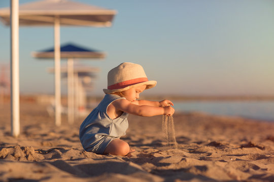 kid in a hat playing with sand on the beach by the sea. holidays with children near the ocean