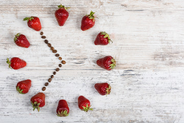 strawberry clock with arrows from coffee beans showing the time 6:55 or 18:55 on a wooden vintage board