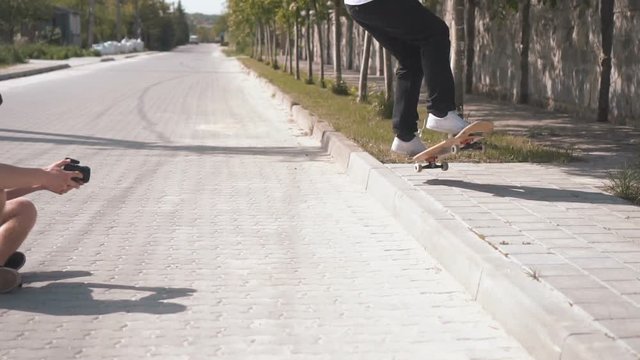 Skateboarder makes jump trick, his friend filming it sitting on longboard, streeet day slowmotion