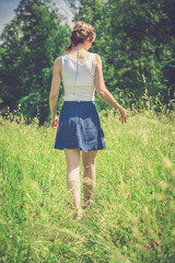 Verträumtes junges Mädchen in grüner Sommerwiese, Rock und Sonnenbrille, Aufnahme von hinten