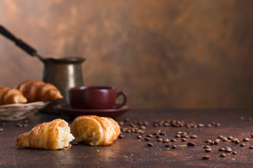 Fresh and tasty croissant  and cup of coffee on old copper background.