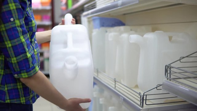 A young woman chooses a large container for liquids in the supermarket. She wants to make a large supply of water or gasoline in her basement. Preparation for natural disasters and man-made disasters.
