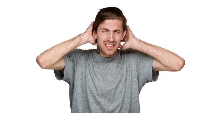 Portrait of tall caucasian guy covering ears and screaming because of annoying noise or loud music, isolated over white background. Concept of emotions