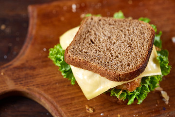 Fototapeta na wymiar Tasty and fresh sandwiches on cutting board over a dark wooden background, close-up