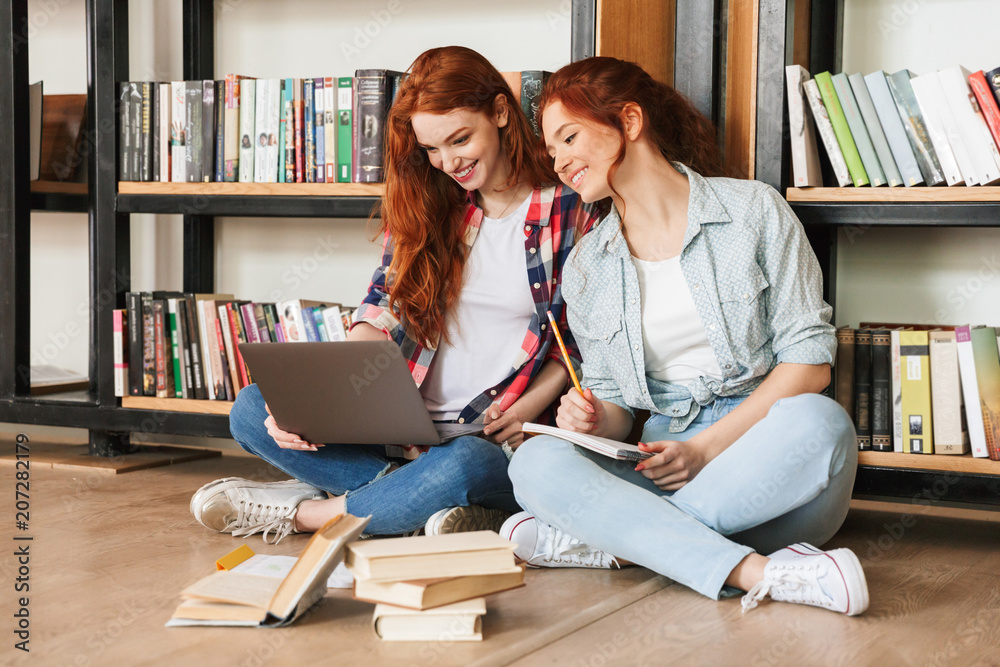 Poster Two smiling teenage girls sitting on a floor at the bookshelf