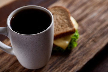 Breakfast table with sandwich and black coffee on rustic wooden background, close-up, selective focus