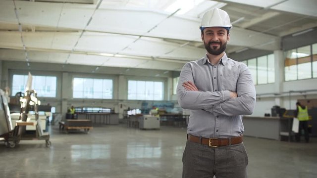 Portrait of adult bearded man, executive manager or engineer, wearing suit and helmet monitoring process of work in factory room slow motion