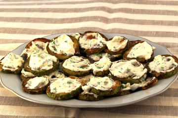 Fried zucchini slices with sauce, sprinkled with finely chopped dill grass.