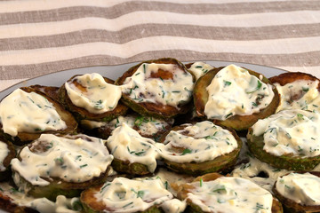 Fried round slices of zucchini with sauce and chopped dill, laid on a plate.