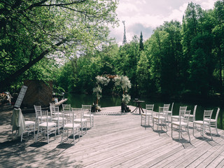 Romantic rustic wedding ceremony near river. White wooden chairs and flower arch
