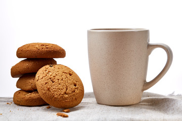 White porcelain mug of tea and sweet cookies on homespun napkin over white background, top view, selective focus