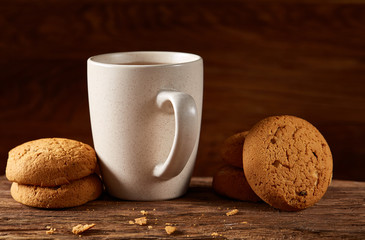 White porcelain mug of tea and sweet cookies on piece of wood over wooden background, top view, selective focus