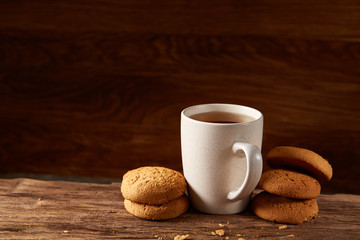 White porcelain mug of tea and sweet cookies on piece of wood over wooden background, top view, selective focus